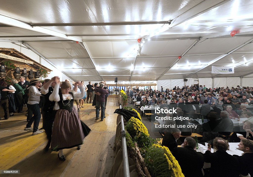 people dancing in entertainment tent at Aelplerfest, Lenk Switzerland "Lenk im Simmental, Switzerland - October 13, 2012: people in traditional Swiss clothing dancing in an entertainment tent at the annual Aelplerfest agricultural show. The tent is crowded with locals and visitors who sit at long tables drinking, eating and listening to various performances of yodel groups and traditional Swiss musical bands." Activity Stock Photo