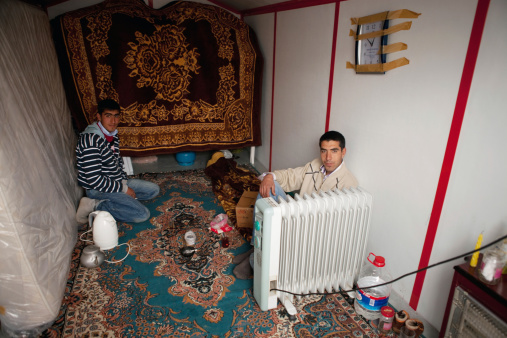 Elazig, Turkey - April 01, 2010 : Young Turkish men drink tea together whilst getting some heat from a plugged-in radiator, inside a temporary house, set up for them by the Turkish Red Crescent - part of the International Red Cross, after the earthquake flattened most of their villages.The 2010 Elazig earthquake was a 6.1 Mw earthquake that occurred on 8 March 2010, almost flattening entire villages in the province and killing many.