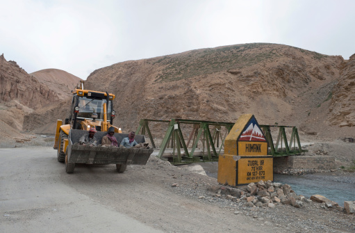 Jugal, Jammu and Kashmir, India - July 23rd, 2011: Three road workers being driven in a digging bucket of an excavator (which has just crossed the Jugal bridge); road Leh Manali, northern India.