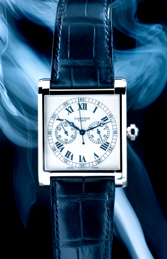Leiden, The Netherlands - September 3, 2008: Product shot of a Cartier Tank Mono Poussoir Collection Privee wristwatch on black background with smoke effects. This watch has a white gold case and an black alligator leather strap. Only one hundred watches were produced, which makes it very exclusive.