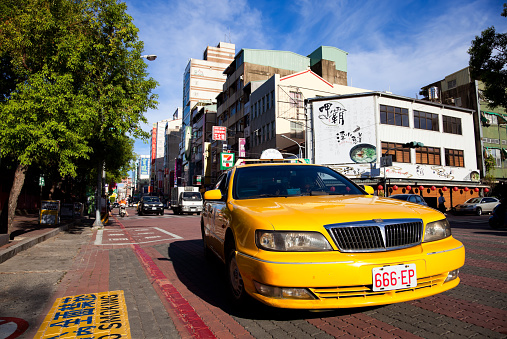 Tainan, Taiwan - June 8, 2011: Asian driver driving a yelow cab in the streets of Tainan on a sunny day. Other vehicles and pedestrians can also be seen.