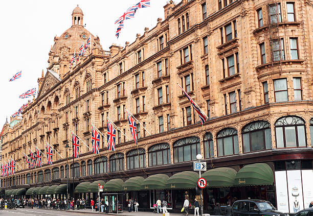 London, United Kingdom - May 5, 2011: Harrods building on Brompton Road in London.  People on the street passing by and looking at shop windows.Sky is almost white due to lighting conditions.