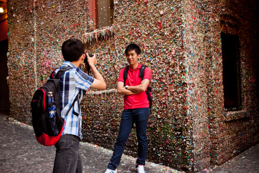 Seattle, Washington, USA - June 17, 2011: A couple of young men stop to take a photo in front of the famous Market Theater Gum Wall in downtown Seattle.  The gum wall is a brick alleyway that is covered with used chewing gum.