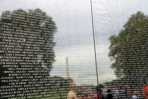 Washington, DC, USA - October 10, 2009: Hundreds of names of casualties of the Vietnam War are etched in this partial view of the Vietnam Veterans Memorial Wall. Reflections of people visiting the memorial are visible in the wall's surface, as well as the surrounding trees and the Washington Monument in the distance.