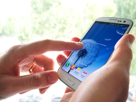 Milan, Italy  October 12, 2012: Business man touching the screen of Samsung Galaxy S 3 android home screen.