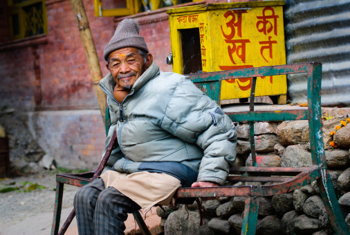 Budanilkantha, Nepal - November 23, 2010: A senior adult male sitting on a metal bench inside the premise of Budanilkantha temple. He has a visible Strauma Grade III Goitre. Worldwide, over 90% cases of goitre are caused by iodine deficiency.