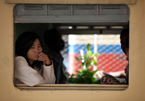Yangon, Myanmar - February 17, 2011: A young woman looks out of a train window thoughtfully as she waits for it to leave Yangon station.The Yangon central railway station is the largest station in Myanmar, the design based on Burmese style architecture. The trains mostly connect only the major cities and are largely government run. There are only two private companies running trains, the quality of which is better than the government run trains.