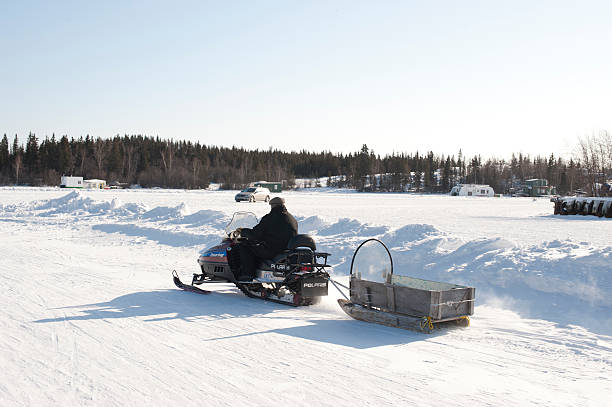 Snowmobiler. Yellowknife, Canada - March, 9 2011: A man drives his snowmobile with a sled attached on Yellowknife Bay.  Yellowknife Bay is part of Great Slave Lake in the Northwest Territories.  Sleds such as this carry spare fuel, camping gear or passengers. great slave lake stock pictures, royalty-free photos & images
