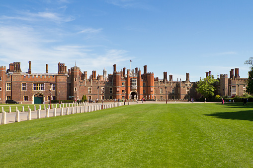 London, United Kingdom - May 3, 2011: Visitors enjoy Hampton Court Palace on a sunny day. It was originally built from 1514 for Cardinal Wolsey but passed back to King VIII in 1529. The house has not had a royal british family living in it since the 18th century. In the following century the palace was expanded and renovated. The palace is an interesting mix of both Tudor and Baroque of two architectural styles. Today is a popular tourist attraction and is cared for by an independent charity. Here people are visiting the castle on a sunny day.