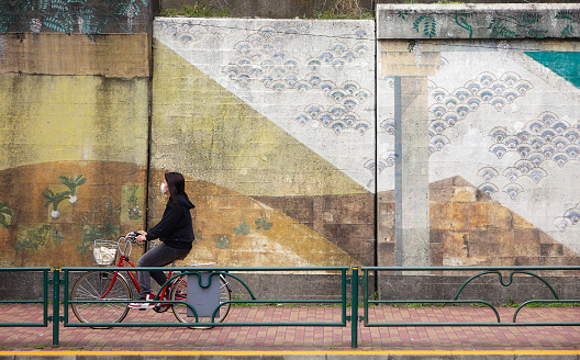 Tokyo, Japan - May 31, 2011:  A woman wearing a surgical mask rides a bicycle past the Kameido train station in the Koto Ward of Tokyo. Wearing a mask in public is a common practice in Japan as a way to minimize the spread of contageous germs.