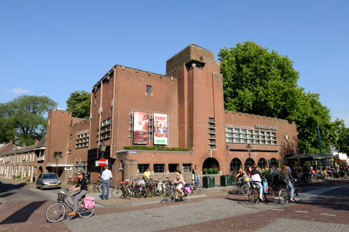 Utrecht, the Netherlands - June 14, 2011: The cinema and culture center Louis Hartlooper Complex (LHC) in Utrecht. The building used to be a police office and was built in 1926. In front of LHC at the right side of the image, people are sitting outdoors, enjoying drinks and food served by LHC. Cyclists are passing by. Cycling is a common and popular method of transportation in the Netherlands.
