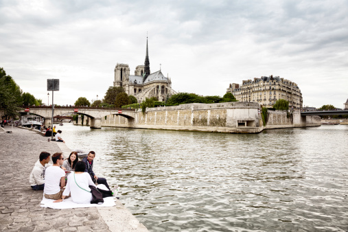 Paris, France - September 7, 2013: Young people are having a picnic on the left bank of the Seine river in view of Notre-Dame and the Ile de la cite.