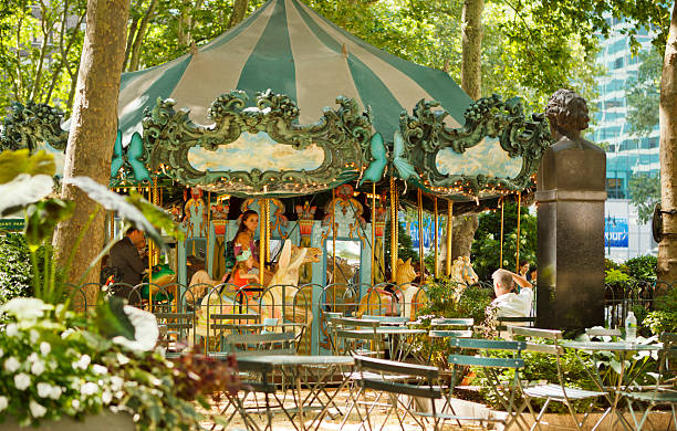 New York, New York, USA - June 30, 2011: Le Carrousel in Bryant Park in Manhattan. People can be seen on the carousel as an onlooker watches. Bryant Park sits behind the New York Public Library on 6th Avenue between 40th and 42nd streets. This carousel sits just off the main open grassy area of Bryant Park.