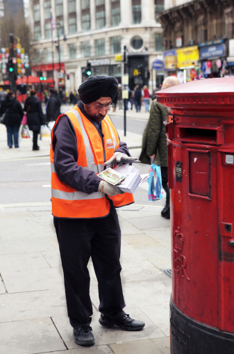 London, United Kingdom - March 5, 2011: A postal worker wearing a turban and Royal Mail Uniform collects post from a traditional red postbox in London\\'s Picadilly Circus.