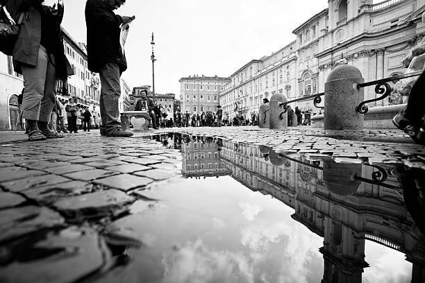 Rome, Italy- October 26, 2011: People reflected on a puddle in Piazza Navona. The square is built on the site of the Stadium of Domitian.