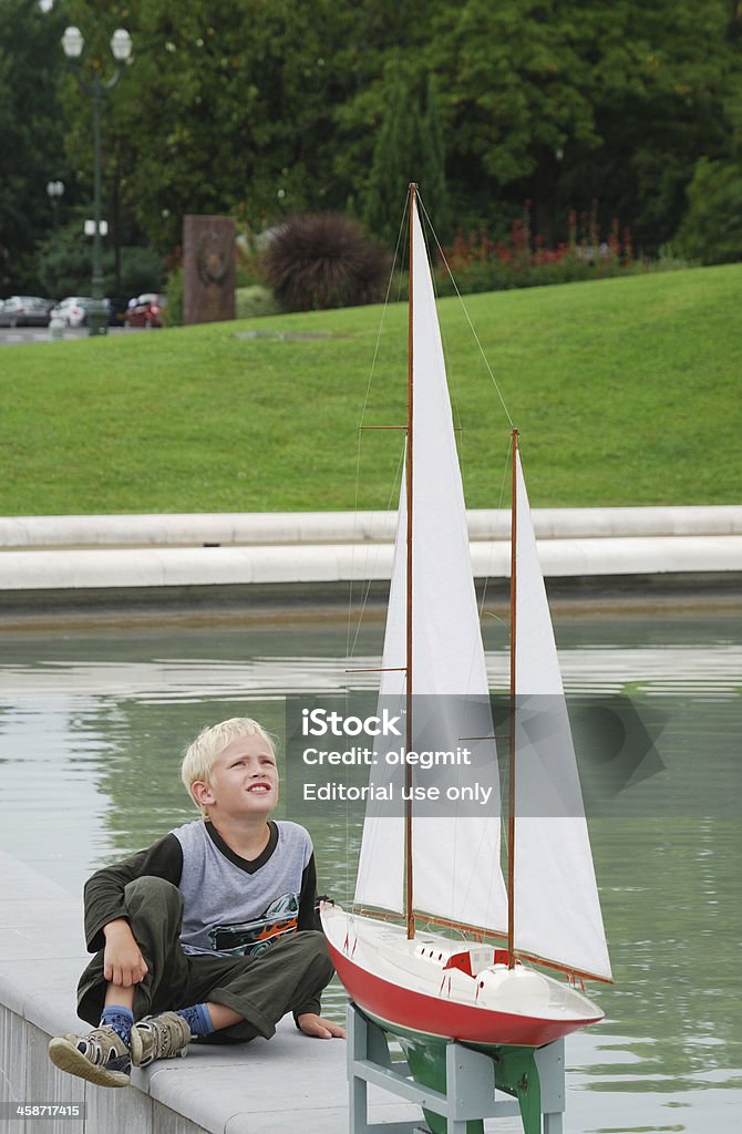 Preteen boy looking at the model yacht. "Pau, France - August, the 7th 2011: The preteen boy intently looks at the model yacht near the pool. Makers of boat model get together near the pool in the central park." Boys Stock Photo