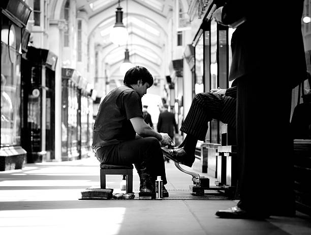 London, UK - May 4, 2011: A young man working as a shoe shiner in the Burlinton Arcade in London, polishes the shoes of a well dressed older gentleman as other shoppers walk past or wait in line to have their shoes polished.