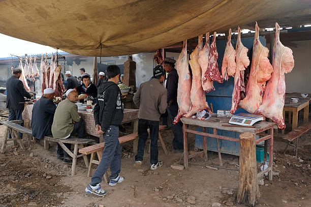 Animal bodies at market in Kashgar "Kashgar, China - October 2, 2011: Outdoor restaurant at animal market in Kashgar. Sheep's bodies hanging, ready to be coocked. ""Zhongxiya Shichang"" or in Uyghur ""Yekshenba"" bazaar is very popular Sunday animal market in Kashgar. It attracts villagers, nomads and tourists." chinese ethnicity china restaurant eating stock pictures, royalty-free photos & images