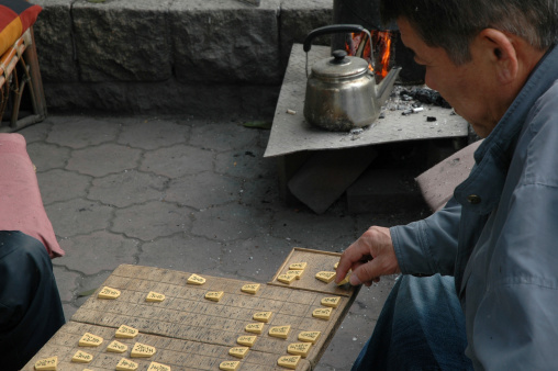 Osaka, Japan--April 7, 2005: Two older men are playing shogi, a Japanese board game not unlike chess, in a public park with their fire burning nearby.