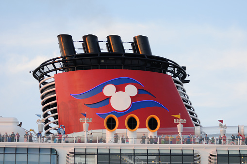 Port Canaveral, Florida, USA  -  November 24, 2012: Passengers stand on deck near the distinctive smokestack of the  cruise ship Disney Fantasy. The Mickey Mouse logo is lit by blue neon lights.