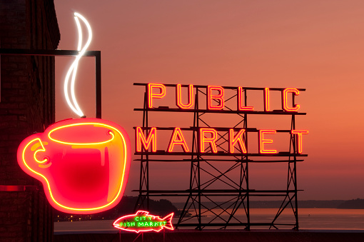 Seattle, USA &ndash; September 11th 2011: Neon Seattle&rsquo;s Best Coffee cup in the foreground of the famous neon Public Market sign at Pike Place Market at sunset.  