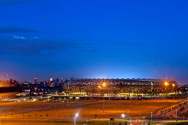Soccer City / FNB Stadium, Johannesburg Johannesburg, South Africa - April, 28th 2012: FNB Stadium or Soccer City, with Johannesburg city seen in the background, evening sundown. Built in the shape of a calabash for the 2010 FIFA World Cup and seats approximately 95000 people. Kaiser Chiefs are playing Supersport. soweto stock pictures, royalty-free photos & images