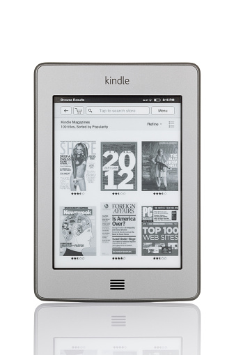 Sofia, Bulgaria - January 2, 2012: Studio shot of reading device Kindle Touch from Amazon.com, supported with WiFi. Isolated on white background with reflection. On the screen are shown popular magazine covers