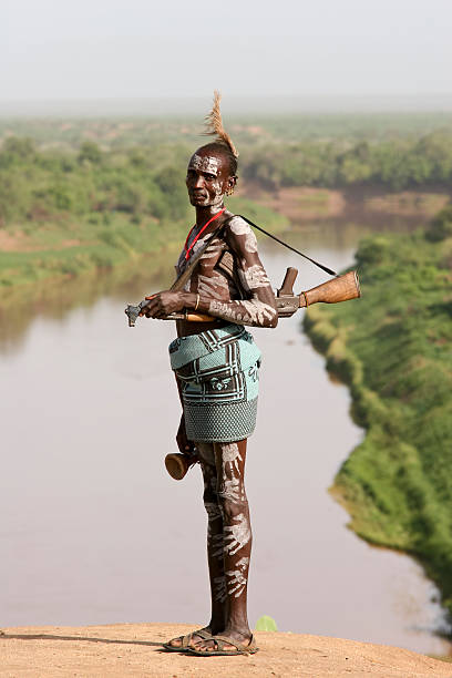 Karo Tribe Man With The Rifle "Omo Valley, Mago National Park, Ethiopia - March 14, 2010: Mid-adult man, member of the Karo tribe protecting the village with the rifle. In the background famous river Omo. The Karo (or Kara), with a population of about 1000 - 1500 live on the east banks of the Omo River in south Ethiopia." omo river photos stock pictures, royalty-free photos & images