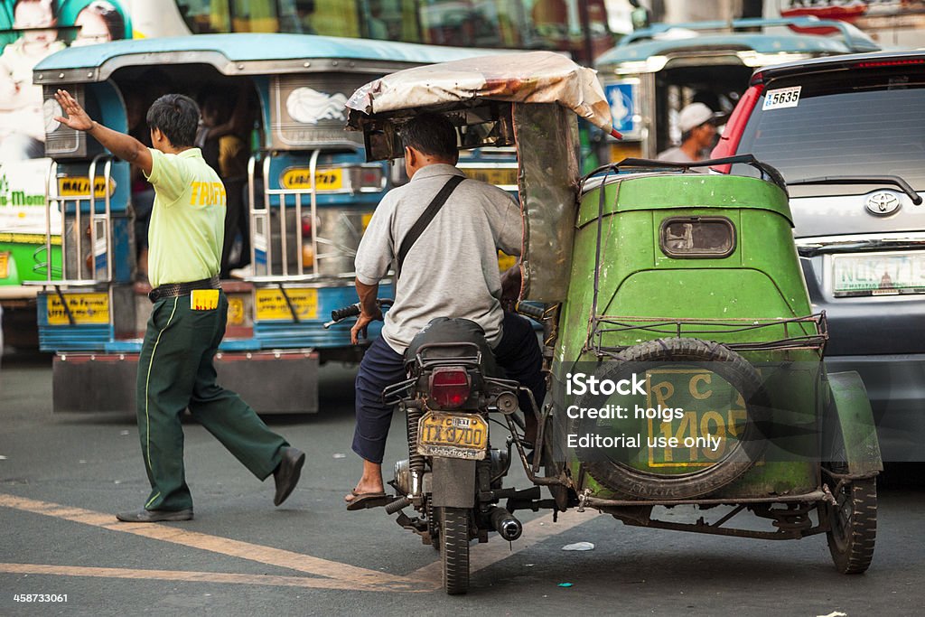 Tricycle in Metro Manila "Manila, Philippines - April 19, 2012: Driver on a motorcycle rickshaw known as a ""Tricycle"" in Metro Manila. An officer directing traffic and a Jeepney can be seen in the background." Makati Stock Photo