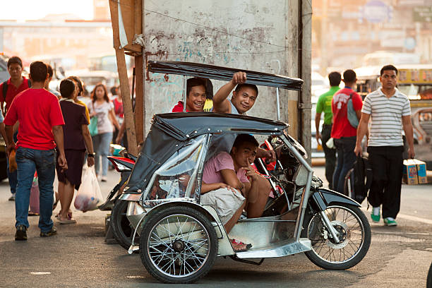 Motorcycle rickshaw known as a &quot;Tricycle&quot; in Metro Manila "Manila, Philippines - April 19, 2012: Driver and passenger on a motorcycle rickshaw known as a ""Tricycle"" in Metro Manila people and a Jeepney can be seen in the background." philippines tricycle stock pictures, royalty-free photos & images