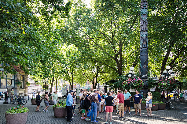 Tour group gathers in Pioneer Square "Seattle, United States - August 9, 2013: A tour group gathers in Pioneer Square on a sunny, summer day in front of the Tlingit totem pole." pacific northwest totem poles stock pictures, royalty-free photos & images
