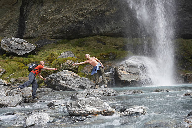 istock Hiker Extending Arm To Friend Under Waterfall 458799759