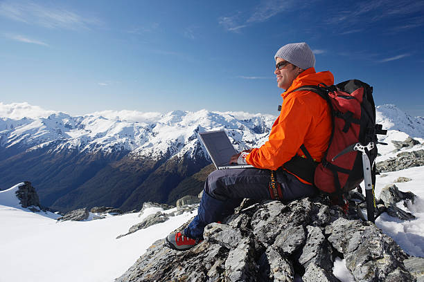 Mountain Climber Using Laptop On Peak stock photo