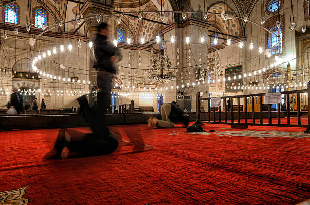 Istanbul, Turkey - November 27, 2010: Muslim people are praying in one of the landmarks of istanbul historical Bayezid II mosque. Two people just right in the middle of namaz and also both standing and sitting figures give idea about how to pray in Islam religion.