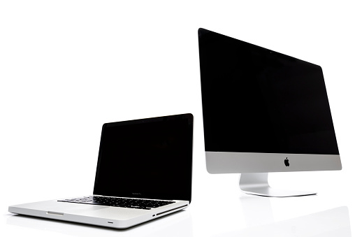 Kampen, The Netherlands - August 20, 2013: Apple iMac desktop computer and Macbook Pro notebook isolated on a white background with a soft reflection in the foreground.