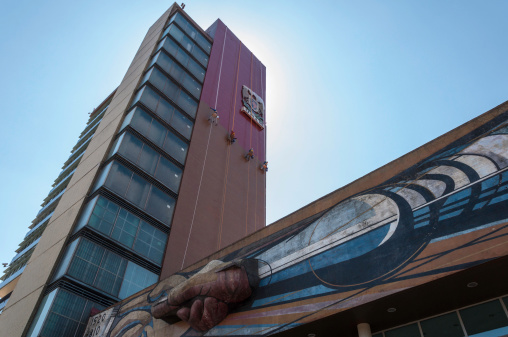 Mexico City, Mexico - March 24, 2013: Dramatic view of the UNAM (Universidad Nacional Autonoma de Mexico) Rectory Building.At top, painters hung on the wall.A detail of David Alfaro Sequiros (1896-1974) mural painting, at bottom.