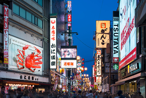 Osaka, Japan - November 25, 2012: Crowds walk below lit signs in Dotonbori. With a history reaching back to 1612, the district is now one of Osaka's primary tourist destinations featuring several restaurants.