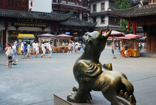 Shanghai, China - August 7, 2013: Yuyuan Bazaar in the Old Town (Nan Shi, Southern City) of Shanghai. A bronze Chinese mythical hybrid creature - a Pixiu - winged lion - is watching an American coffee shop (Starbucks) across the street.