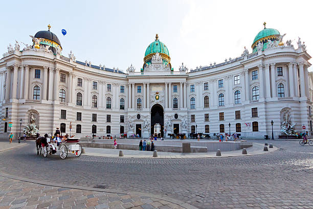 Hofburg Palace, Imperial Apartments, Vienna. Vienna, Austria - June 19, 2013: Hofburg Palace, Kaiserappartements. The Hofburg Palace is a complex of palaces that has been expanded over the centuries. Hofburg was a winter residence of the Habsburg dynasty, rulers of the Austria-Hungary empire. Wide angle view backlit by an evening sun. Tourists are walking around and riding in horsedrawn carriage. habsburg dynasty stock pictures, royalty-free photos & images