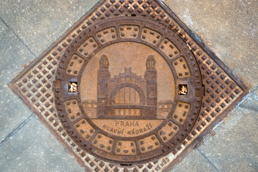 Prague, Czech Republic - July 5, 2013: A manhole cover with an attractive design and Czech texts on the street in Prague. Cigarette butts are caught in two indentations.