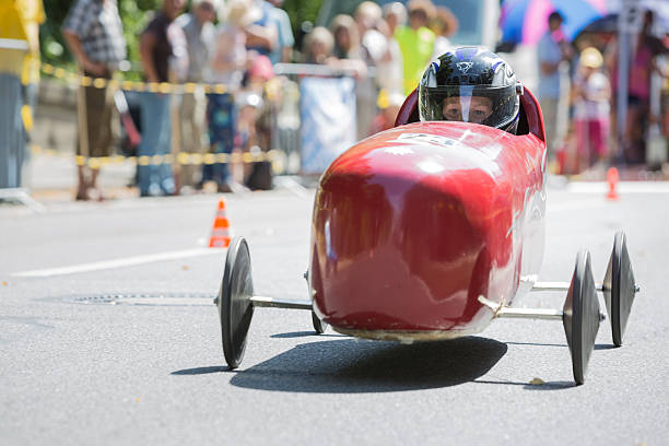 Soapbox car race in Munich Munich, Germany - July 28, 2013: Each year there is a soapbox car race down the Gebsattelberg (small hill within Munich). Locals are competing for the funniest and fastest vehicles. A boy with a helmet sitting in a red cigar shaped racing car. People cheering at the barriers to the track. soapbox cart stock pictures, royalty-free photos & images