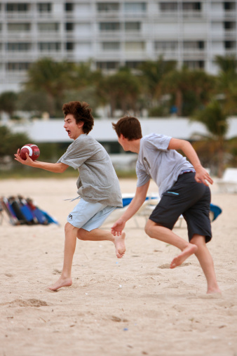 Ft. Lauderdale, FL, USA - December 29, 2012:  An unidentified teenage boy catches the ball while another boy defends, in a touch football game on the beach of a Ft. Lauderdale hotel.