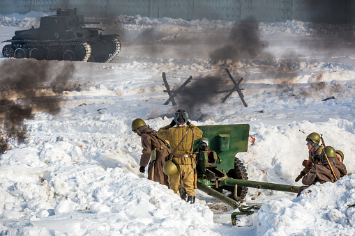 Kubinka, Moscow region, Russia - February 23, 2013: Fascist tank attacking Russian infantry. Soviet gun firing on the enemy.  Soviet gun is 76 mm divisional gun M1942 (ZiS-3). Fascist tank is LT vz.38 (Panzerkampfwagen 38(t), Pz.Kpfw.38(t)). Reconstruction of the Second World War battle with the participation of tanks, armored vehicles and infantry. The battle is going on in Military-historical museum of  armored vehicles and armament of Main auto-tank directorate of Defense ministry of Russian Federation known  as 