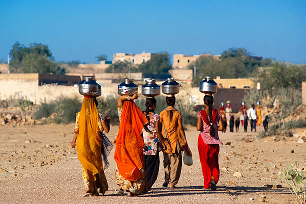 Rajasthan, India - February 27, 2013: women lugging a water pot on their head. Due to the lack of piped water, poor tribals have to fetch water from its natural sources.