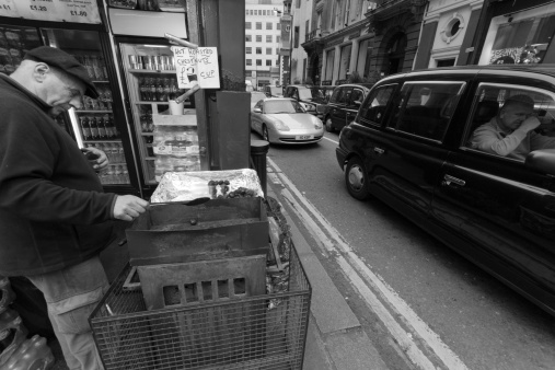 London, United Kingdom - January 4, 2013: Chestnut vendor on a street corner off Ocford Street London, He is putting the chestnuts in a plastic container whilst a black cab driver sits next to him in a traffic jam.