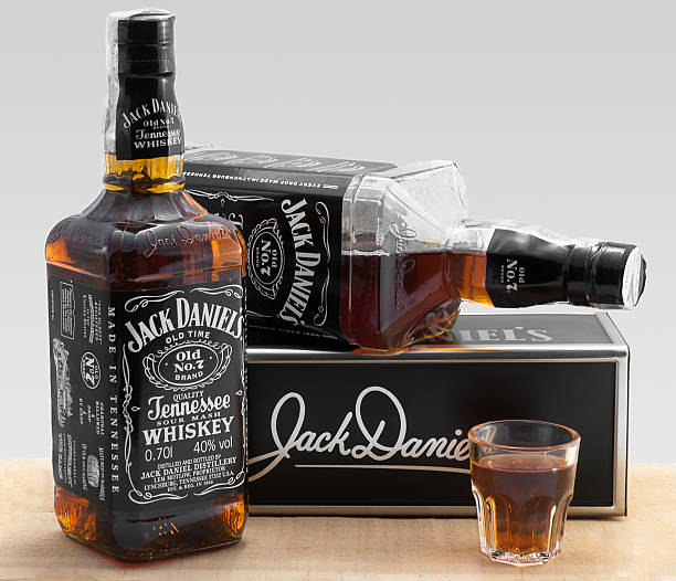Pistoia, Italy - March 9, 2013: two bottles of Jack Daniel's whiskey and a shot glass full of whiskey, isolated on grey. Label states the whiskey was made in Tennessee, product of U.S.A.