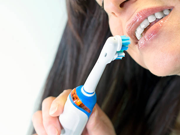 brunette woman brushing teeth with  electric toothbrush stock photo