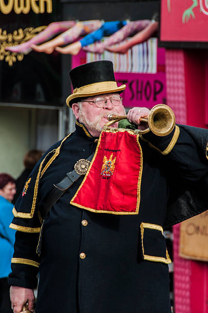 Playing the trumpet London, England, United Kingdom - October 9, 2011: A man of strong build, dressed in the attire of a Coachman from the end of the 19th century, plays the cornet for the attention of the passers and publicize the settlements of Camden Town Market. Over his head, we see the claim of stockings shop. town criers stock pictures, royalty-free photos & images