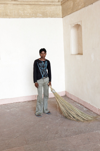 Agra, India - November 19, 2010: Asian man inside bare room in Indian temple with traditional sweeping broom