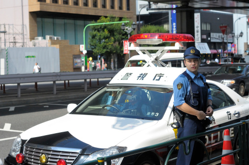Tokyo, Japan - September, 9 2010. Policeman standing in front of the police car. This is one of the cars, standing in the row near Roppongi metro station. The police was likely waiting for some action.